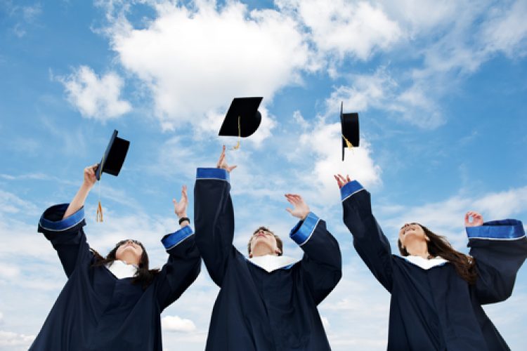 Three graduate students tossing up hats over blue sky